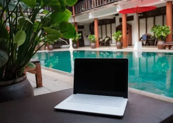Digital nomad working besides pool - a laptop computer sitting on top of a table next to a pool.