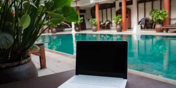 Digital nomad working besides pool - a laptop computer sitting on top of a table next to a pool.