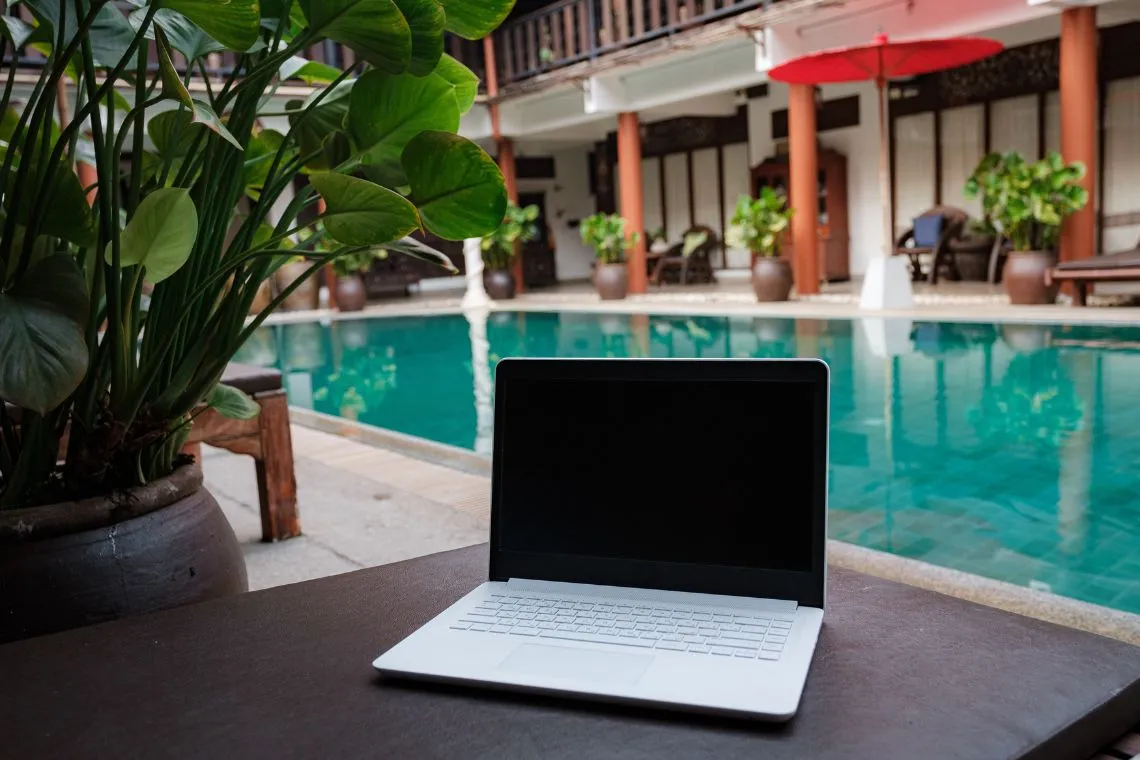 Digital nomad working besides pool - a laptop computer sitting on top of a table next to a pool.