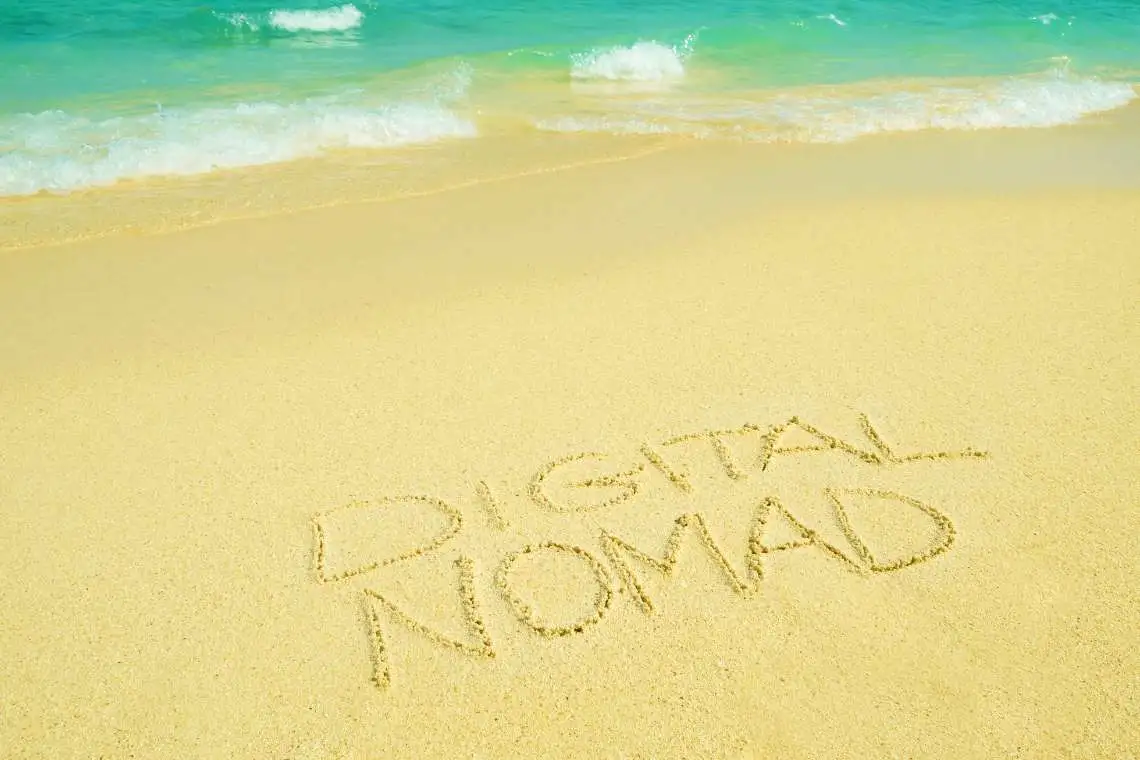 the word digital nomad written in the sand on a beach.