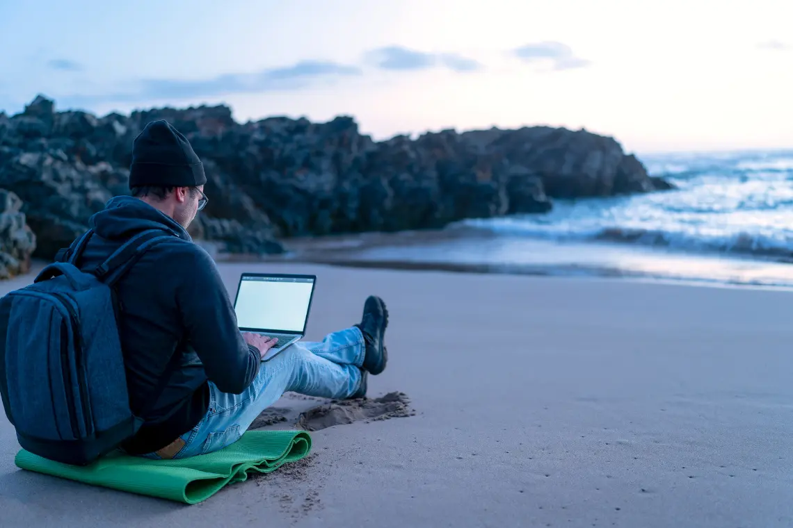 Nomad working on a laptop at the beach, exemplifying remote work flexibility.